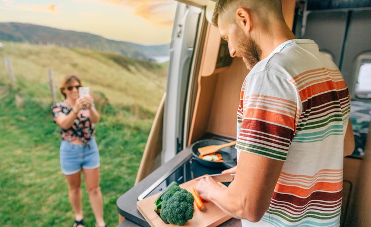 Woman taking picture of male cooking vegetables in motorhome