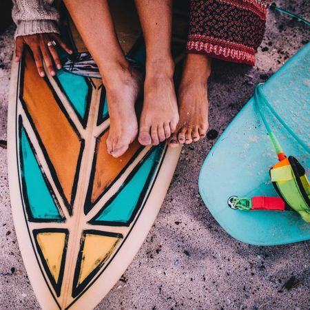 Women’s feet resting atop a patterned surf board in the sand