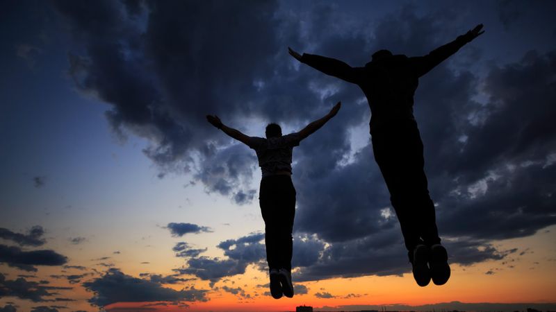 Out line of two men jumping against a colorful dusk side