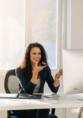 Woman sitting in front of computer in office discussing business on cell phone