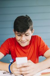 Teenage boy wearing red t-shirt sitting outdoors using phone