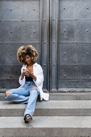 Young Black woman speaking on smartphone while sitting near building