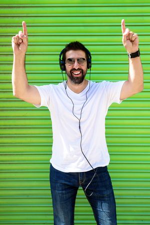 Man in headphones and glasses pointing up in front of green background