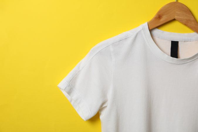 Hanger with blank plain t-shirt on yellow background, space for text