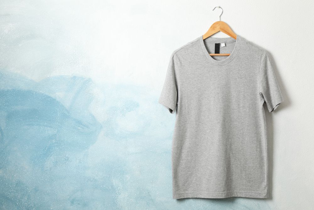 Hanger with blank gray t-shirt on blue background, space for text