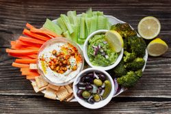Tasty hummus and sauces decorated with bright cut vegetables on table