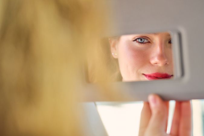 Crop smiling woman looking in car vanity mirror