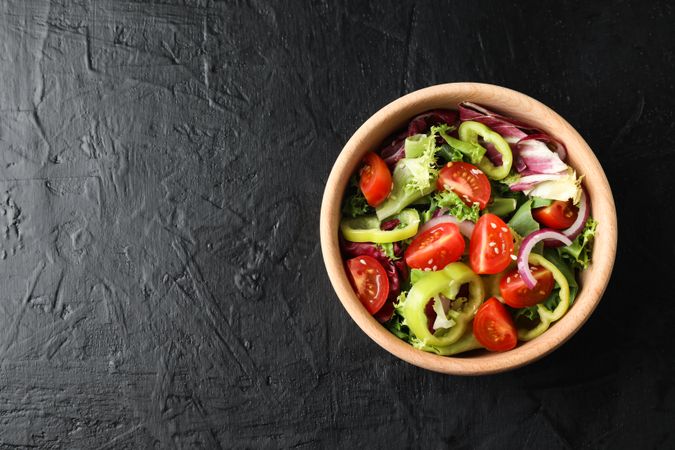 Wooden plate with salad on dark background, top view