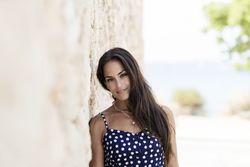 Beautiful hispanic woman in blue dress leaning head on wall and looking at camera