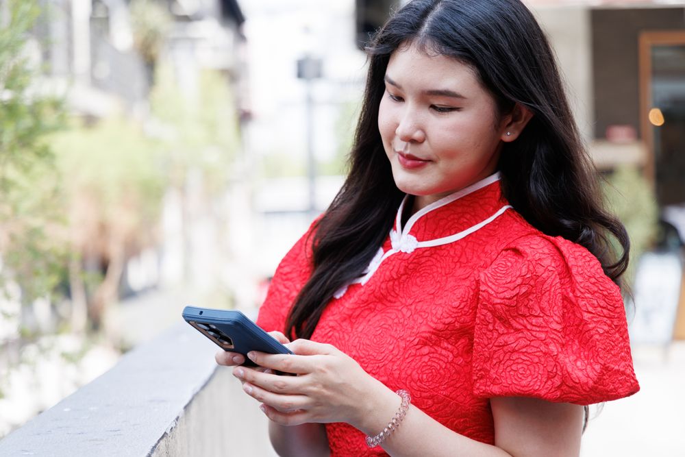 Asian female in red Chinese New Year shirt chatting on mobile phone