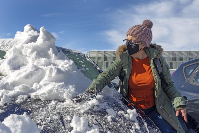 Woman with facemask removing snow off her car's windshield