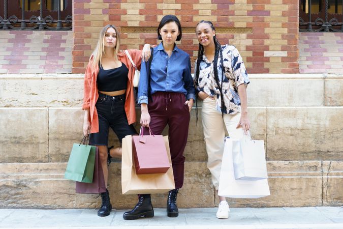 Women standing proudly with shopping bags in front of brick wall