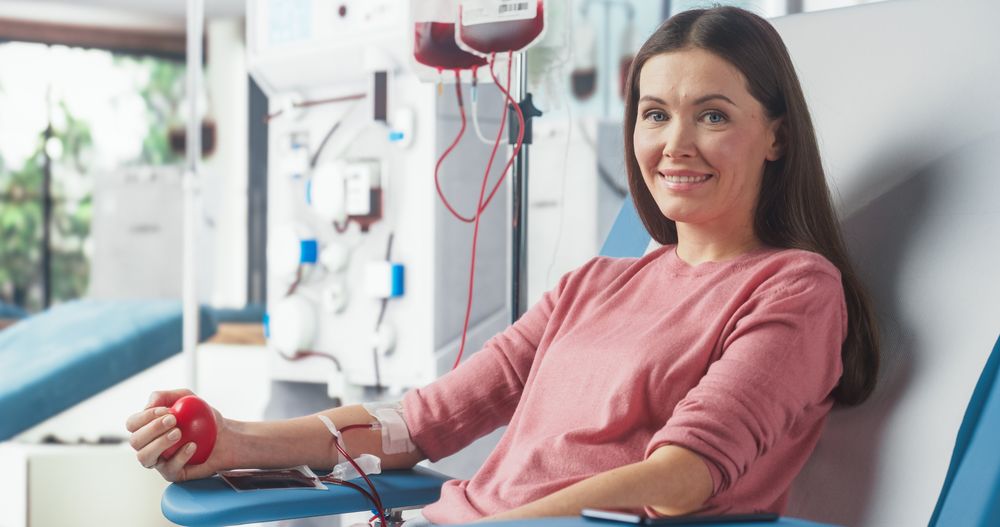 Female Donor Squeezing Heart Shaped Ball To Pump Blood. Looking Into Camera And Smiling.