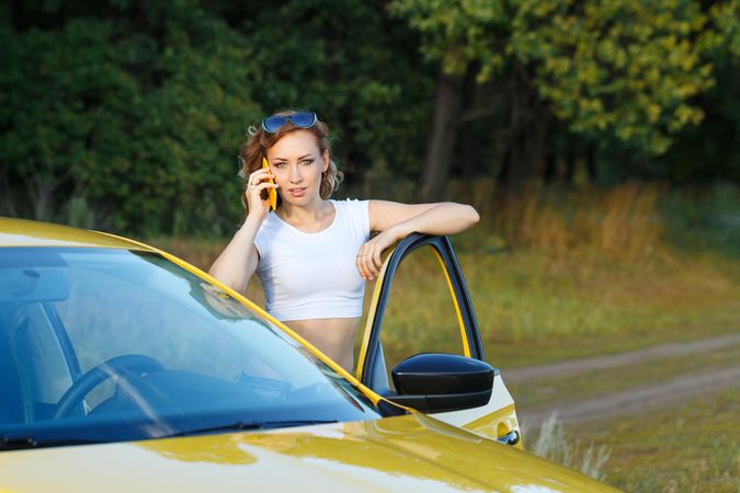 Woman with sunglasses talking on cell phone standing outside of her yellow car
