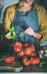 Woman in yellow holding basil, with wire basket of large tomatoes