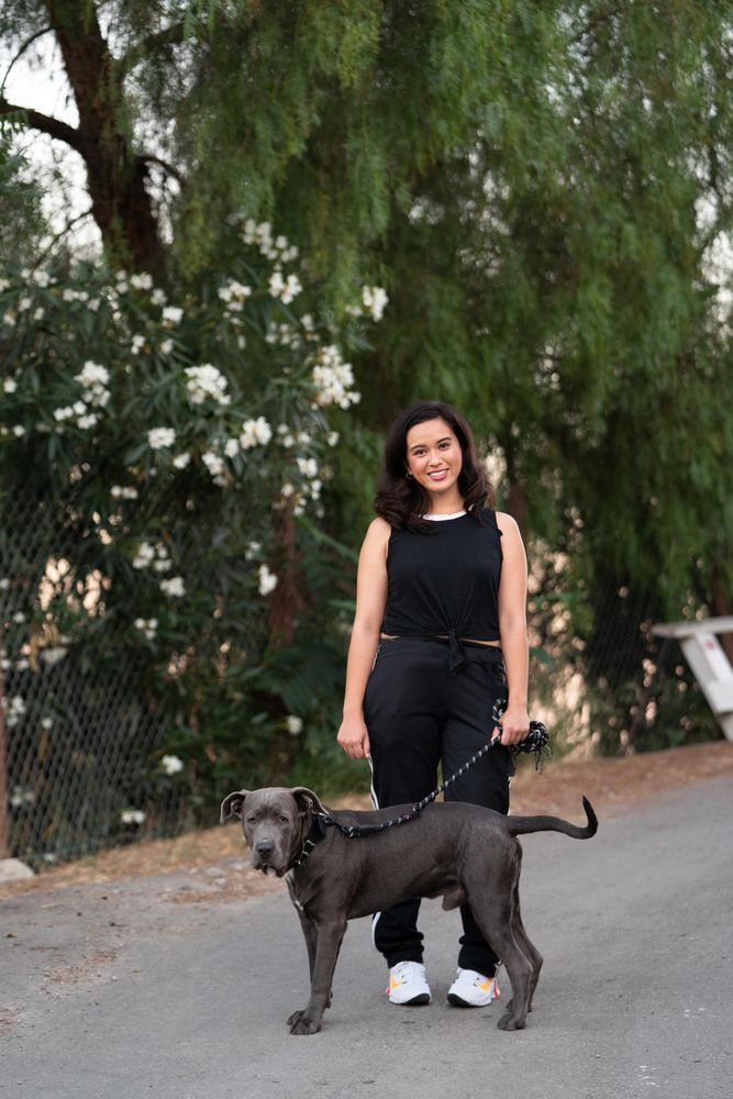 Woman standing in front of green trees on a quiet street with her dog