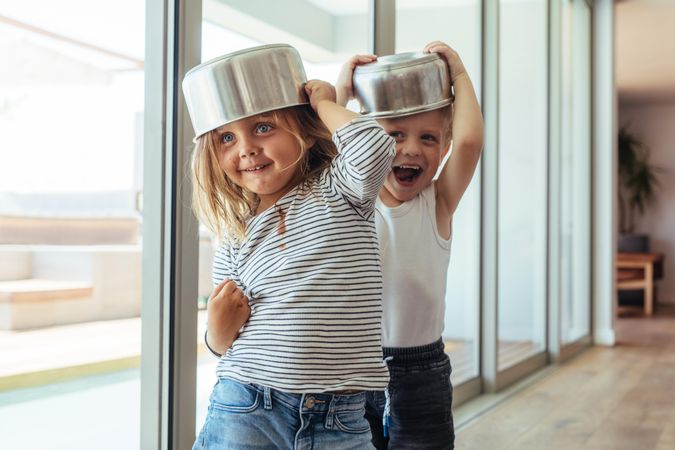 Cute little kids wearing bowls as helmet and playing at home