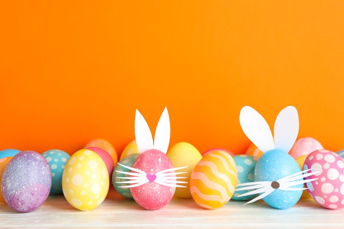 Decorated Easter eggs and cute bunny's ears on table against color background. Space for text