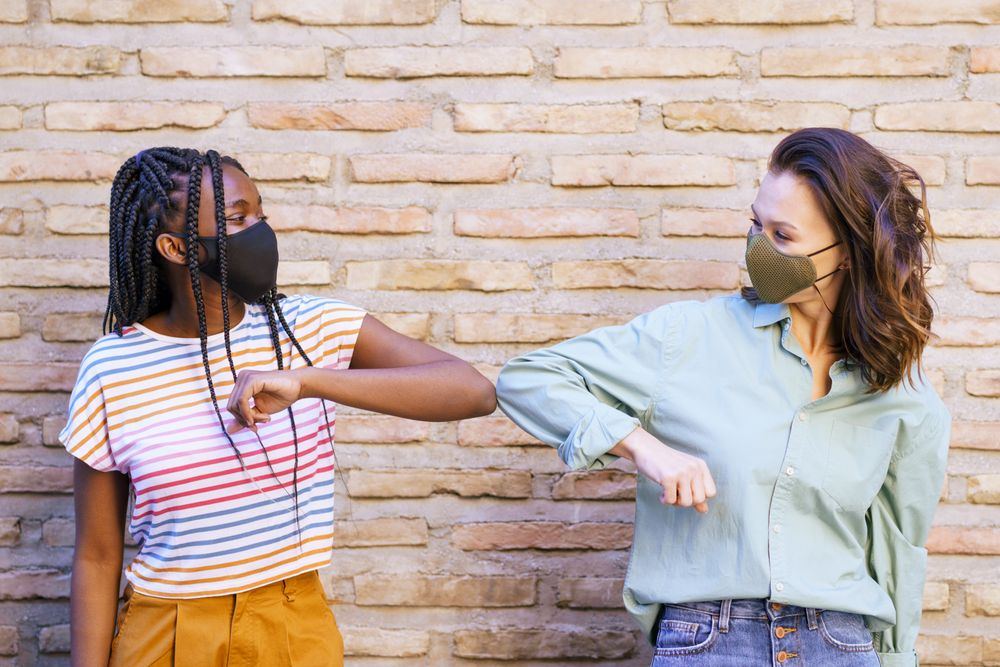 Female friends tapping elbows in lieu of shaking hands protecting themselves from virus outdoors