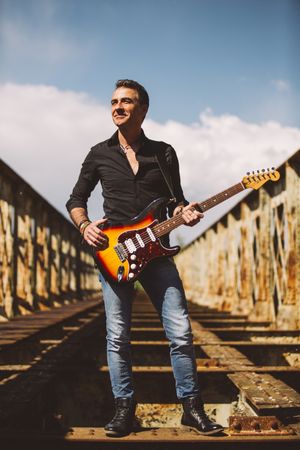 Man with guitar standing on bridge