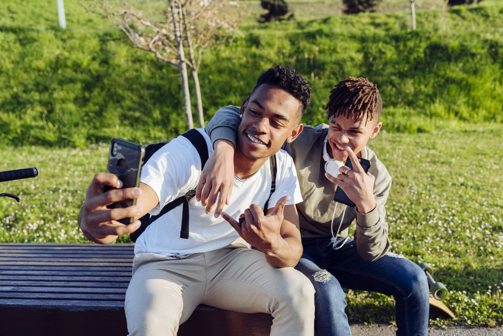 Young Black men sitting on bench with smartphone