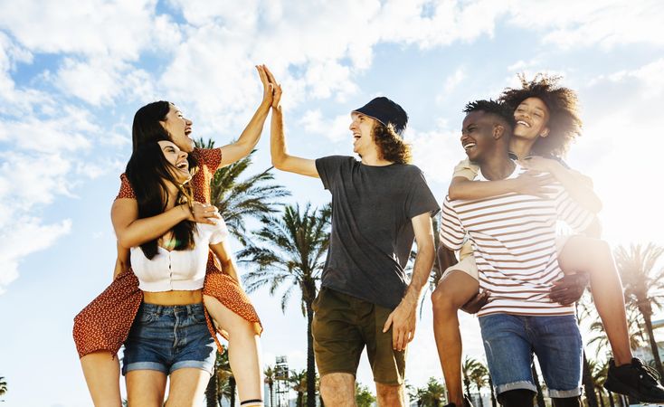 Group of happy multiracial friends celebrating outdoors with back sunlight