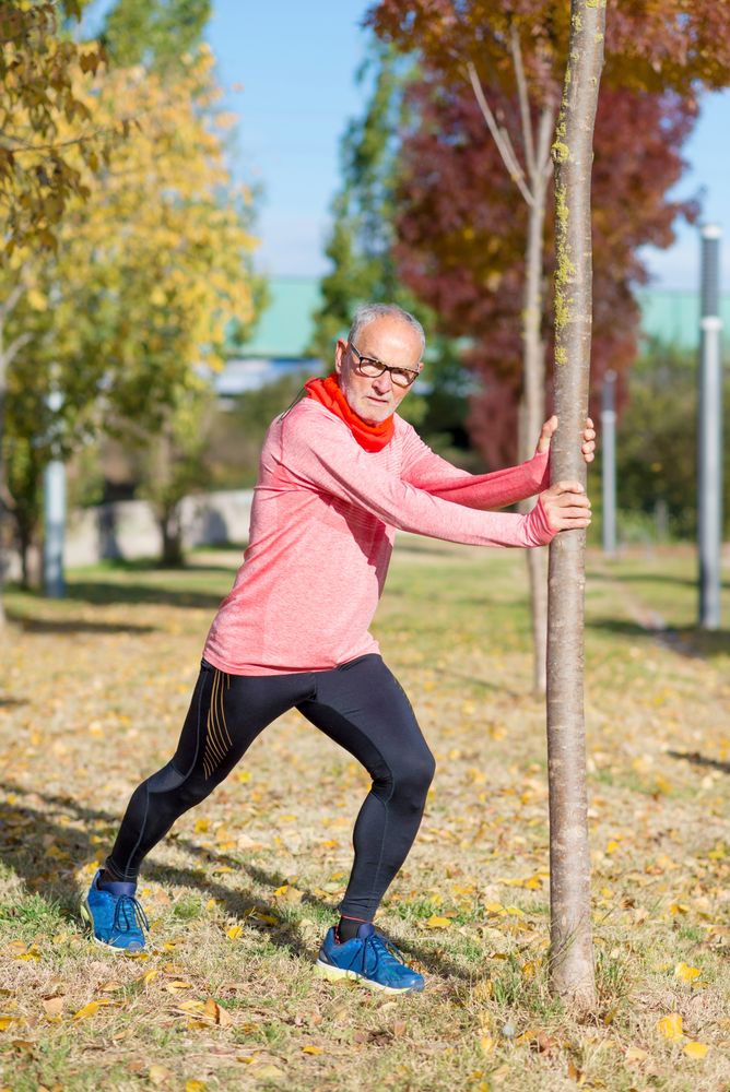 Male stretching legs in park using tree for balance