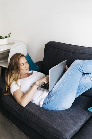 Relaxed woman lying on sofa with laptop computer working remotely from home