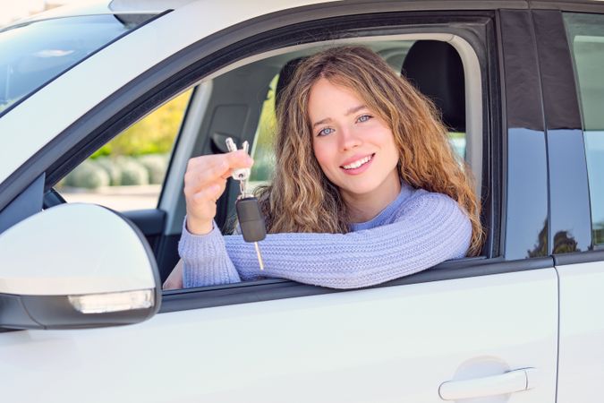 Cheerful woman showing keys and sitting in car