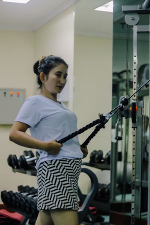 A woman asia is exercising on a cable machine at a gym