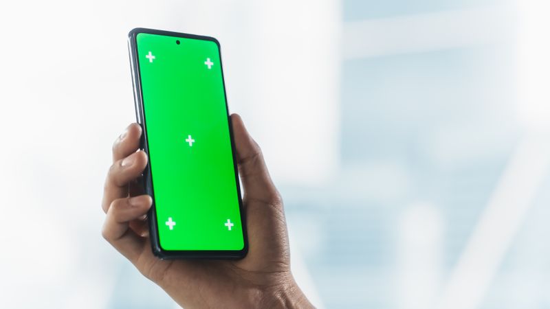 Anonymous Business Person Using Smartphone with Green Screen Mock Up Display for Social Media Posting. Man's Hand Holding Cellphone Vertically with Isolated Area for App, Software, Website Promotion
