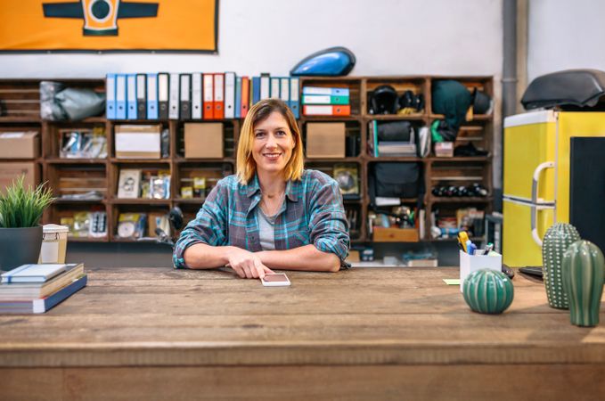 Portrait of smiling blonde young female employee looking at camera behind of industrial shop counter