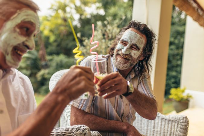 Happy older people toasting juice glasses with facial clay mask on