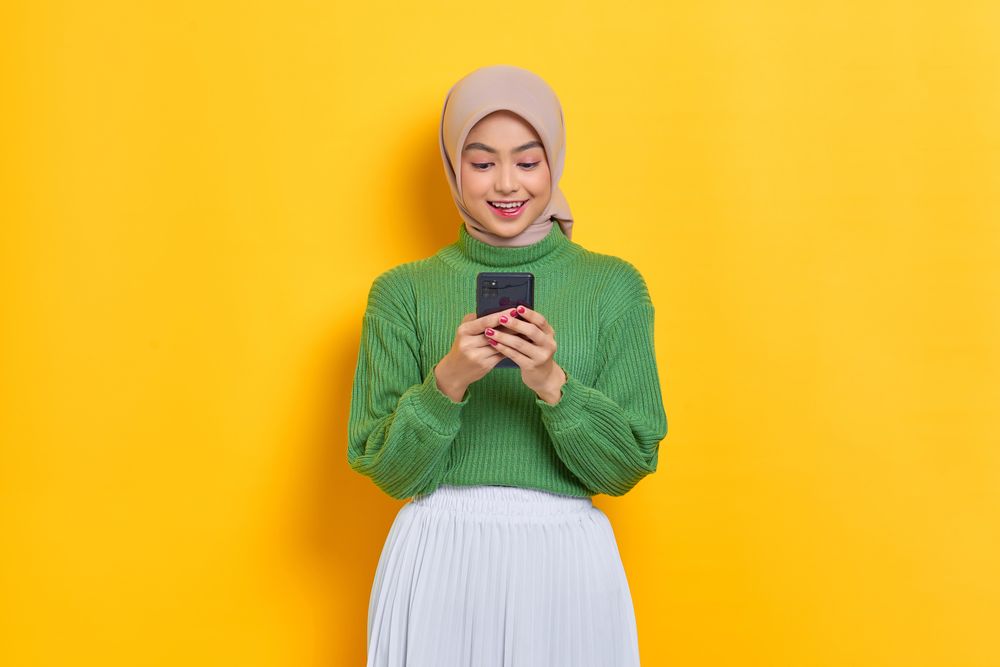 Woman in headscarf smiling and looking down at her smart phone