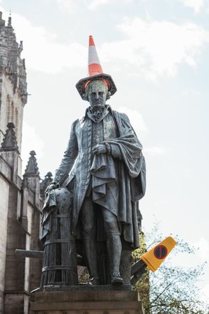 Aged monument with road cone on head