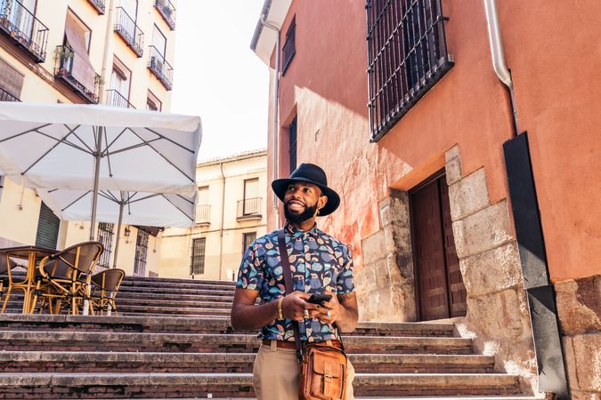Stylish Black man walking on the city street using smartphone