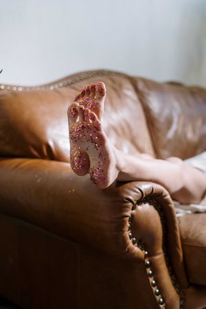 Cropped image of feet with glitter on brown couch