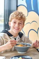 Happy kid tasting Asian soup from bowl in restaurant