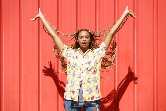 Confident woman holding up her braids in front of a red wall