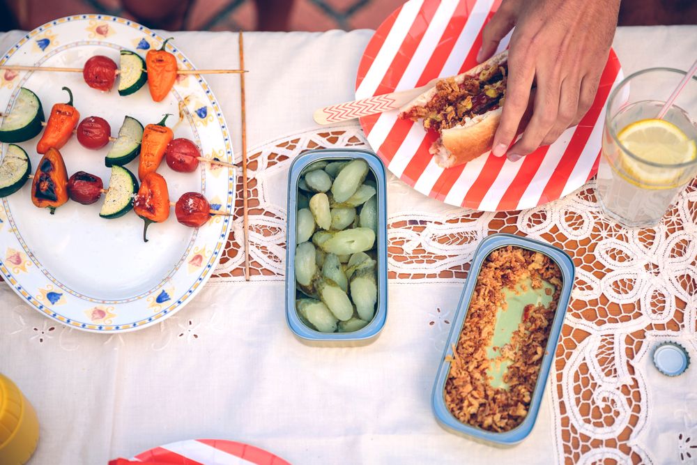Male hand reaching for hot dog on red striped plate