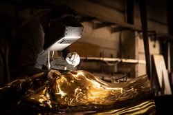 Man in mask welding metal ware in darkness