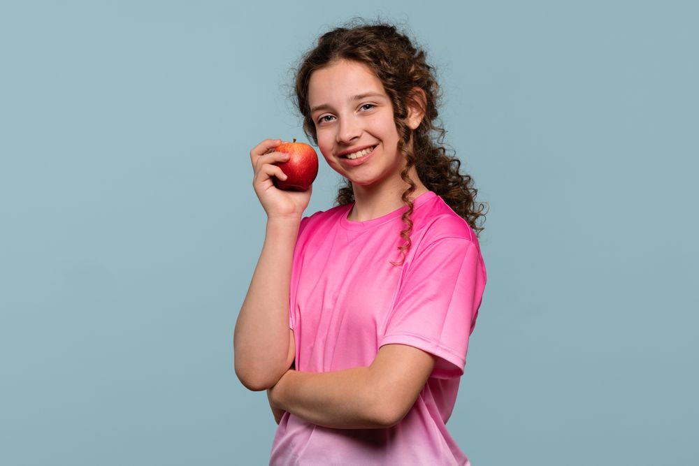 Happy girl holding red apple against cheek.