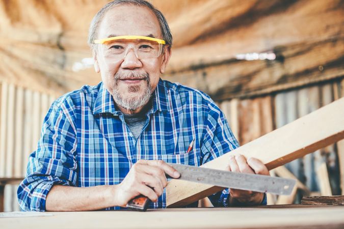Mature man smiling with wood in carpentry shop