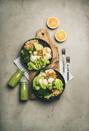 Two vegetarian bowls,  with smoothie, on placemat, bread board, vertical composition