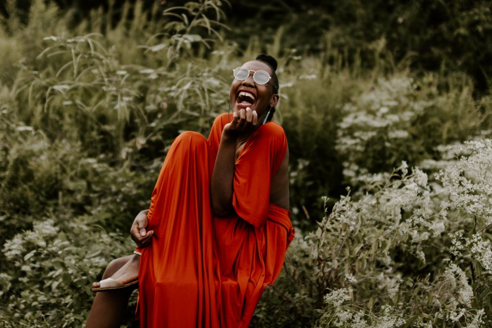 Woman wearing orange dress sitting by green bushes laughing