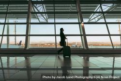 Silhouette of female flight passenger with luggage walking at airport terminal 4dGXL5