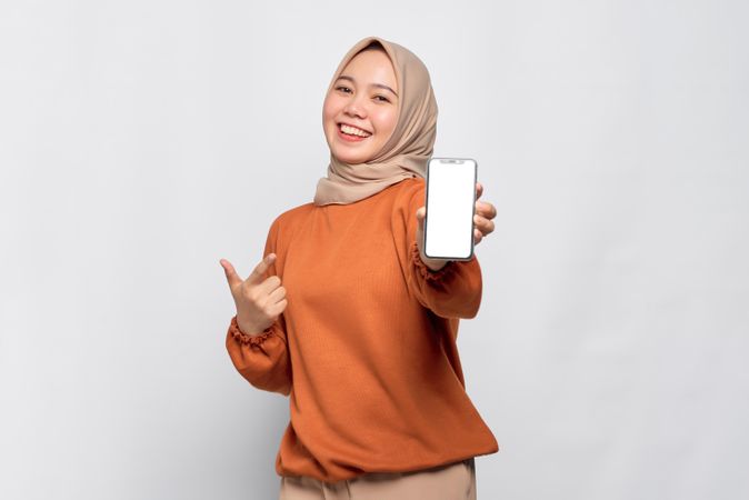 Happy Muslim woman smiling holding smart phone and pointing finger at screen