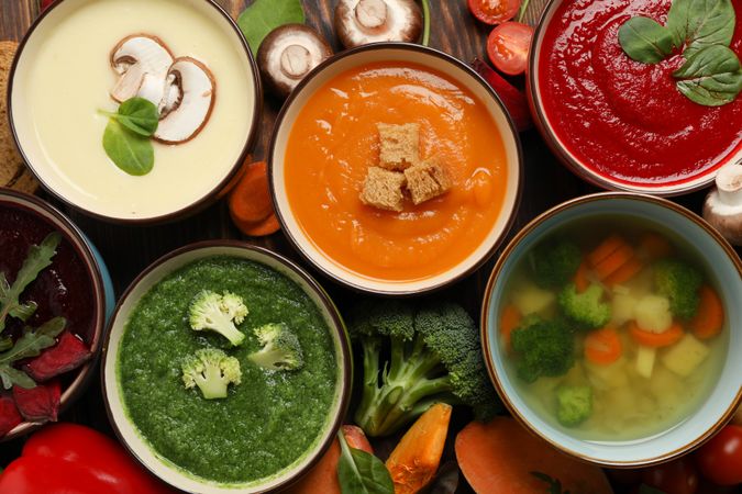Top view of colorful soups and vegetables with on dark wooden table