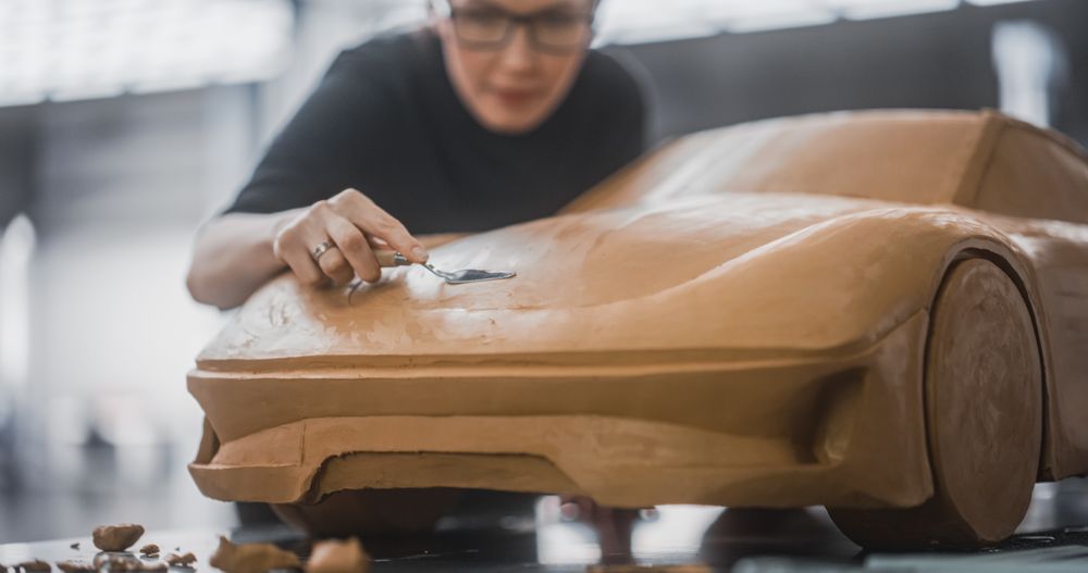 Female Car Modeler Enjoying Creative Work Process on a Concept Car Made Out of Plasticine Modeling Clay.