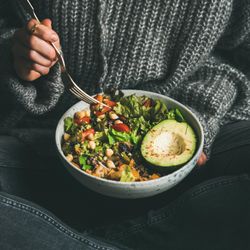 Woman in jeans and sweater eating fresh salad, square crop